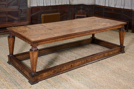 Eglantine table. Oak table with inlaid walnut rectangular top. four conical legs, tapered from top, also inlaid, as is frieze and stretchers with moulded edges. Legs have carved capitals with egg and dart moulding above a gadrooned ring. Plinth foot is squared. Inside of stretchers painted strapwork pattern. Outside diamond and oval pattern. Frieze inlay has metopes and drops with roundels between. Top inlaid with musical instruments, etc.